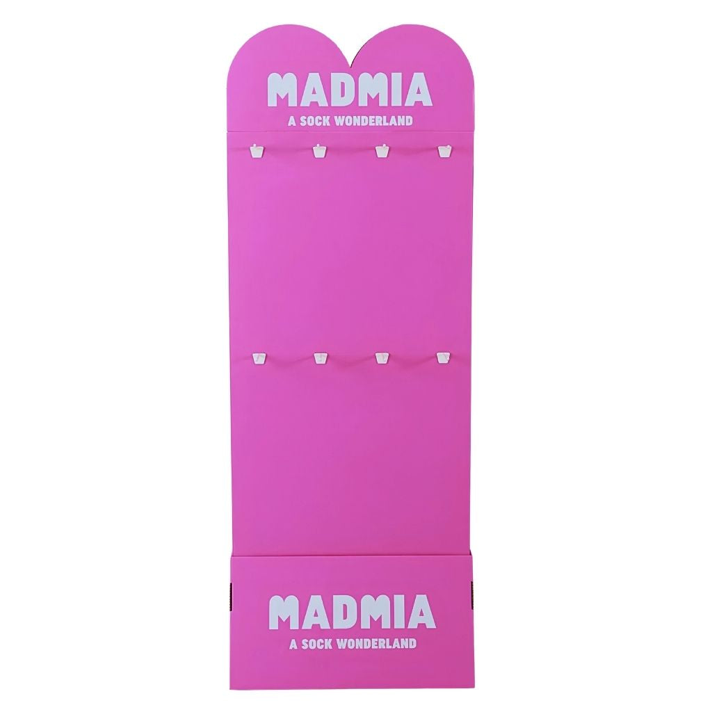 A bright pink cardboard display stand for socks, featuring the brand name 'MADMIA' and the tagline 'A SOCK WONDERLAND' printed in white at the top and bottom, with multiple small white hooks on the front.